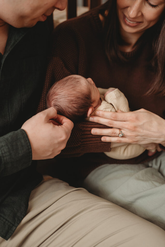 A father and mother sitting closely together, their hands gently resting on their newborn baby to capture the warmth and connection of these first quiet days.