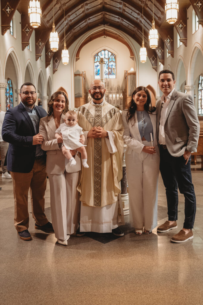 A formal group portrait including the parents, godparents, and priest standing together in the center of the church's stunning architecture.
