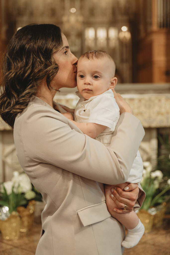 A tender moment of a mother kissing her baby's forehead during the baptism celebration, highlighting the heartfelt emotion and joy of the day.