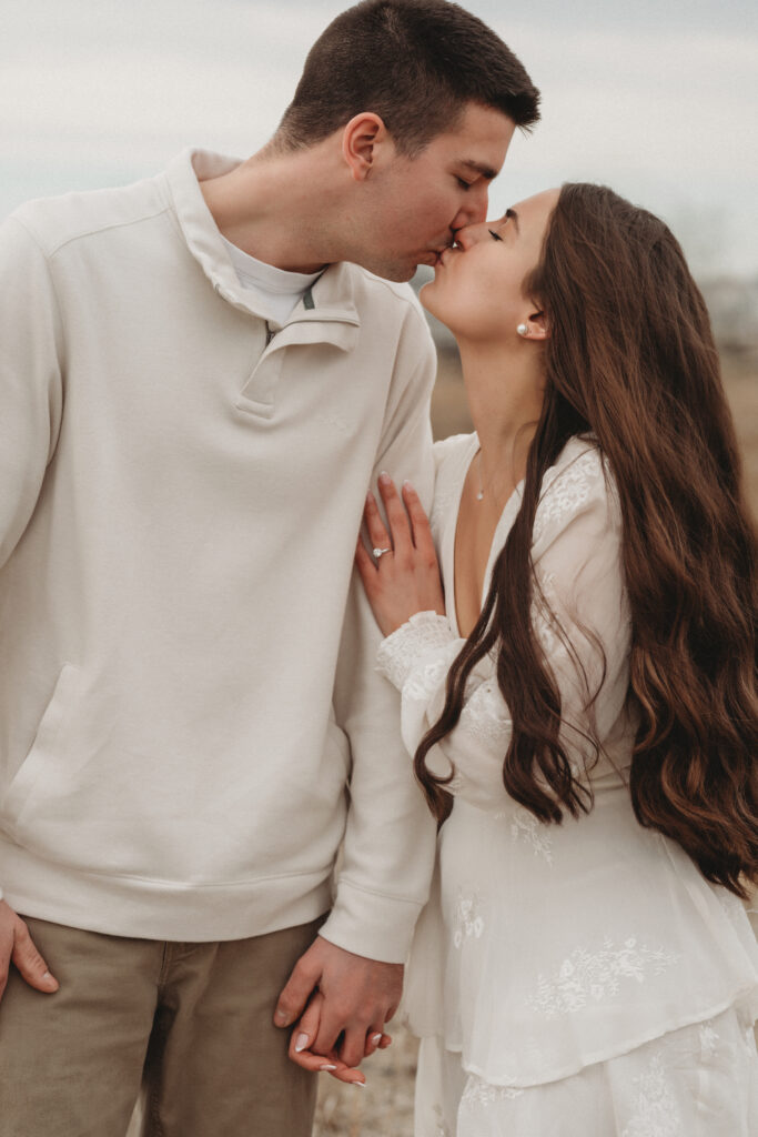 A close-up of Savannah and Joe sharing a kiss during their engagement session, with Savannah wearing a white dress and her engagement ring prominently displayed.