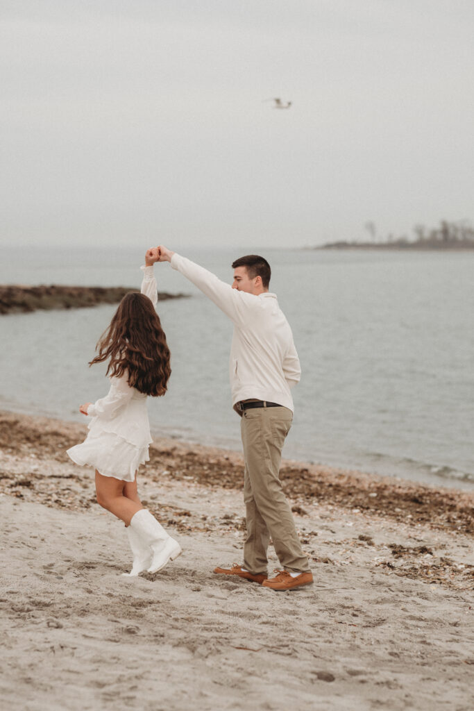 A playful moment of Joe spinning Savannah on the sand by the water, capturing the easy love and movement of their Milford, CT engagement session.