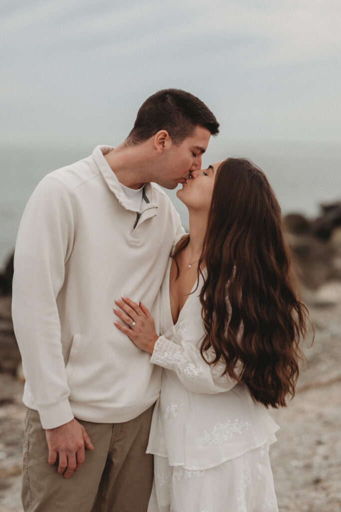 Savannah and Joe sharing a romantic kiss on the rocky shoreline of Milford, CT, during their golden hour engagement session.