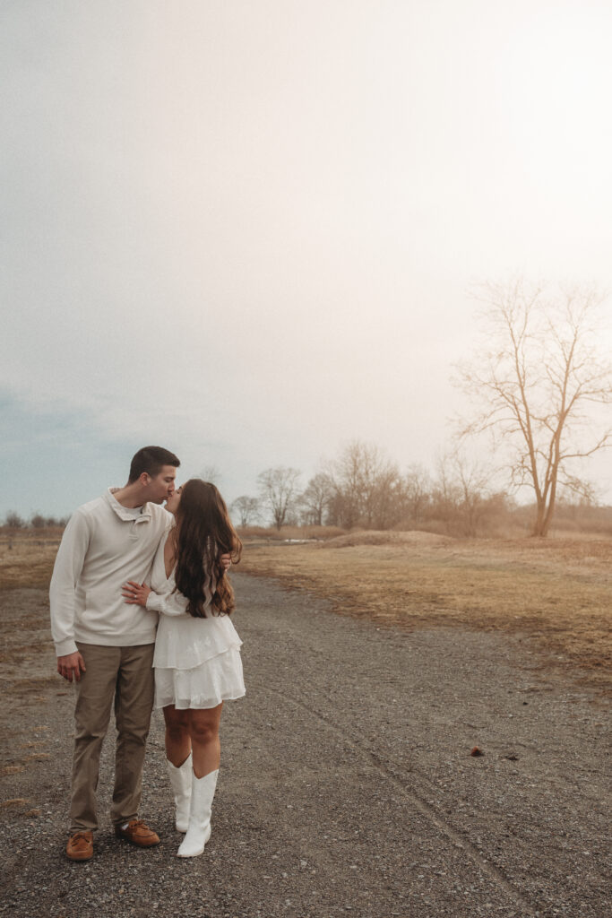 Savannah and Joe sharing a kiss while walking down a gravel path, documenting a quiet and natural moment from their engagement session.