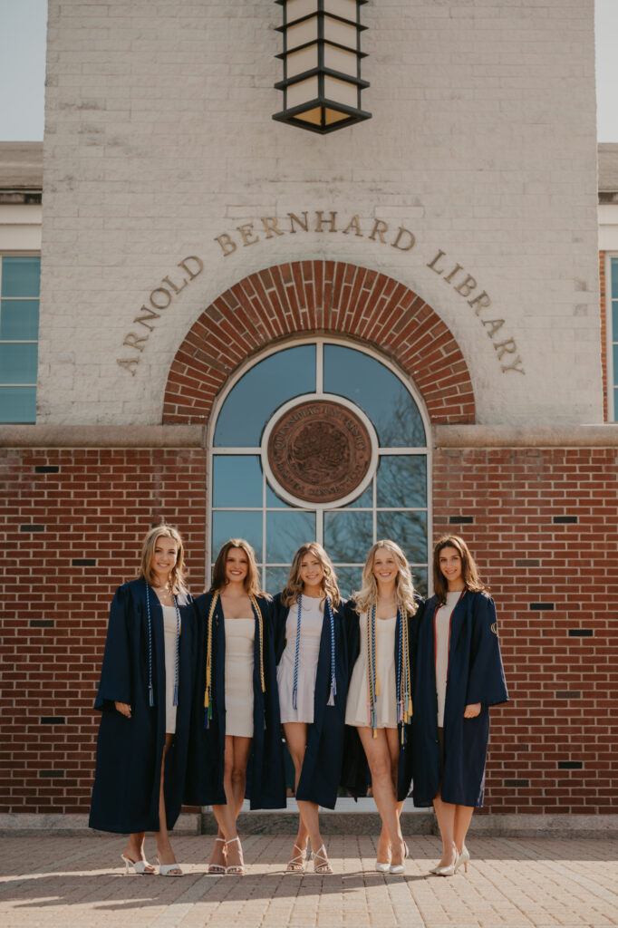 A group of five friends posing in front of the Arnold Bernhard Library at Quinnipiac University, capturing their shared accomplishment and college friendships.