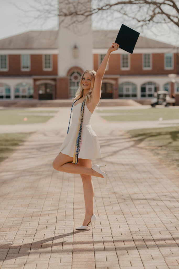 A graduate posing with one leg lifted and her cap raised high, reflecting the excitement and genuine connection of her graduation experience in Hamden, CT.