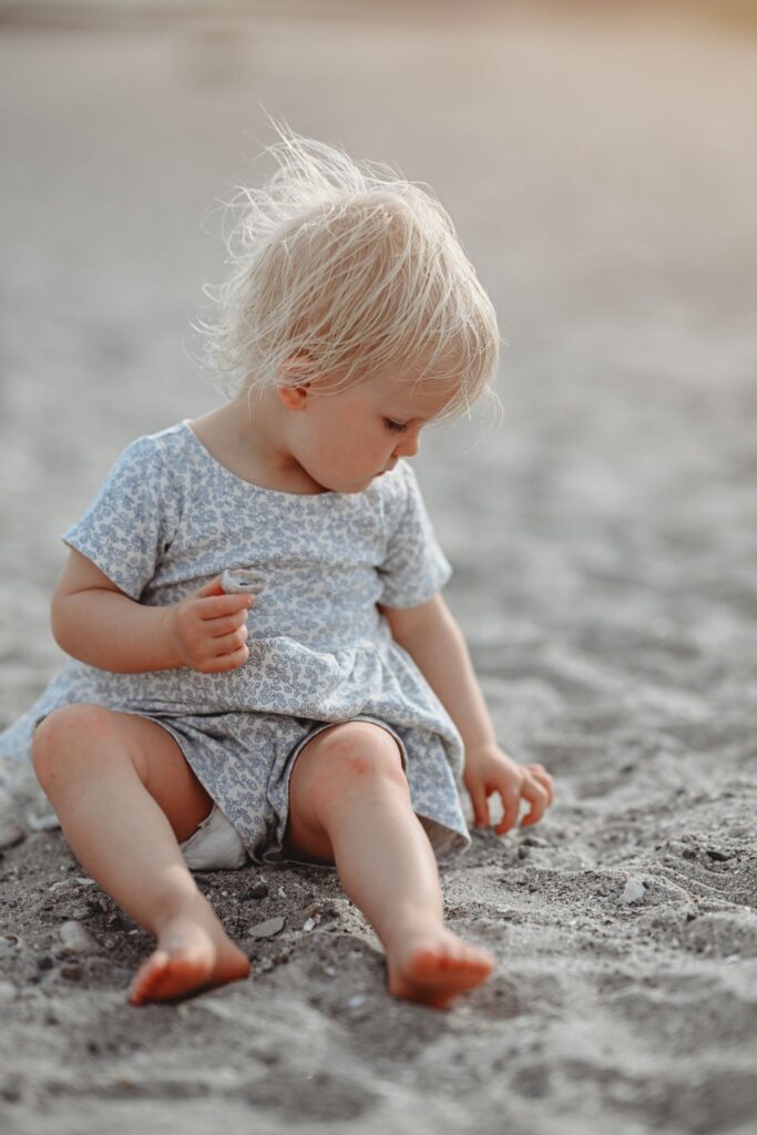Adorable blond toddler boy sitting on the grass in a light patterned romper, captured in a natural newborn-to-toddler milestone portrait.