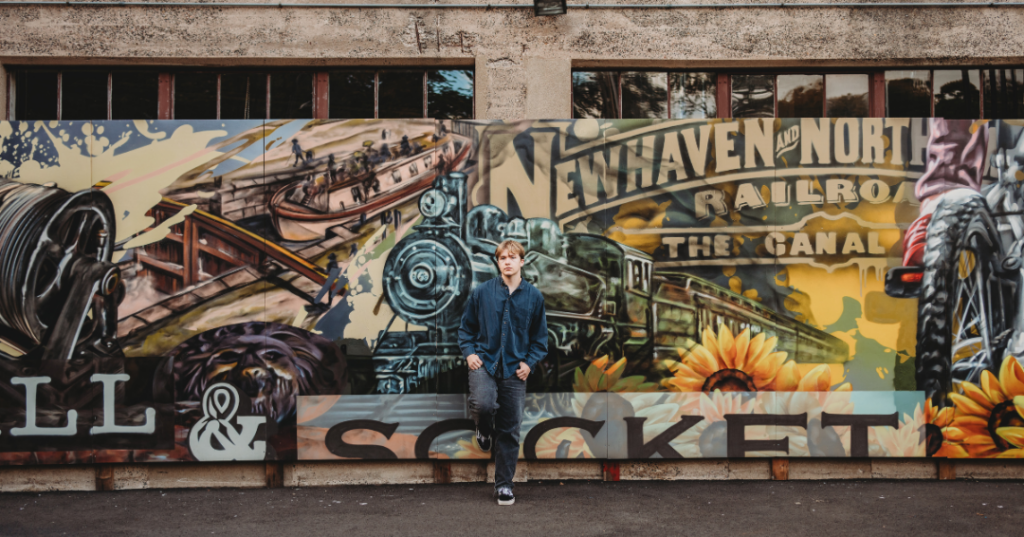 High school senior boy posing in front of a colorful mural featuring New Haven and North Railroad artwork