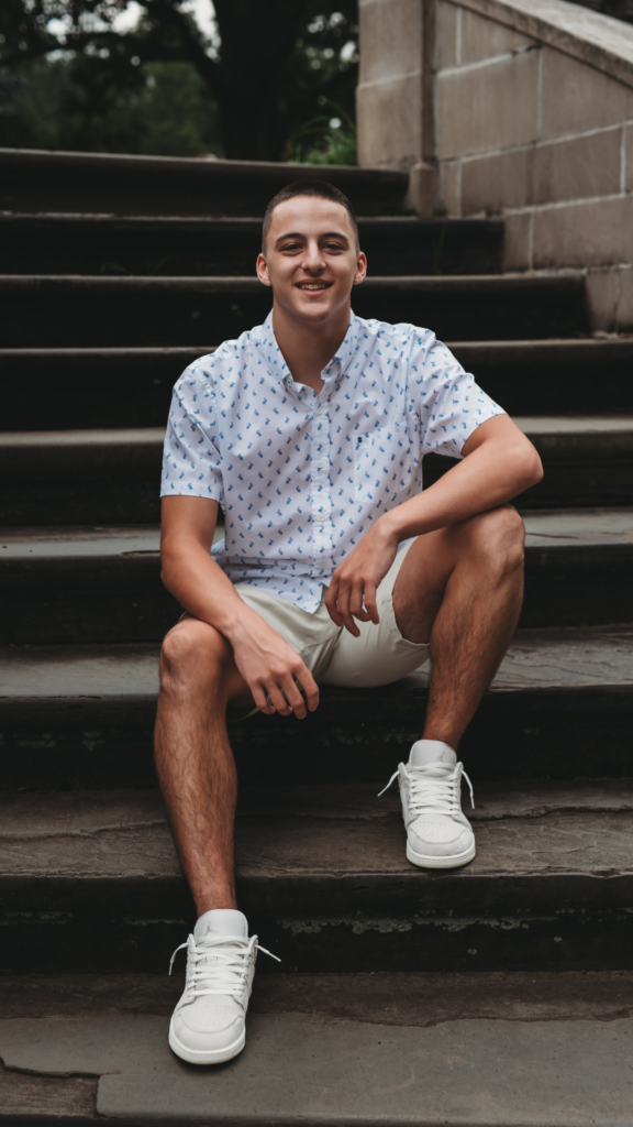 High school senior boy  posing on stone steps in a lush garden in Connecticut