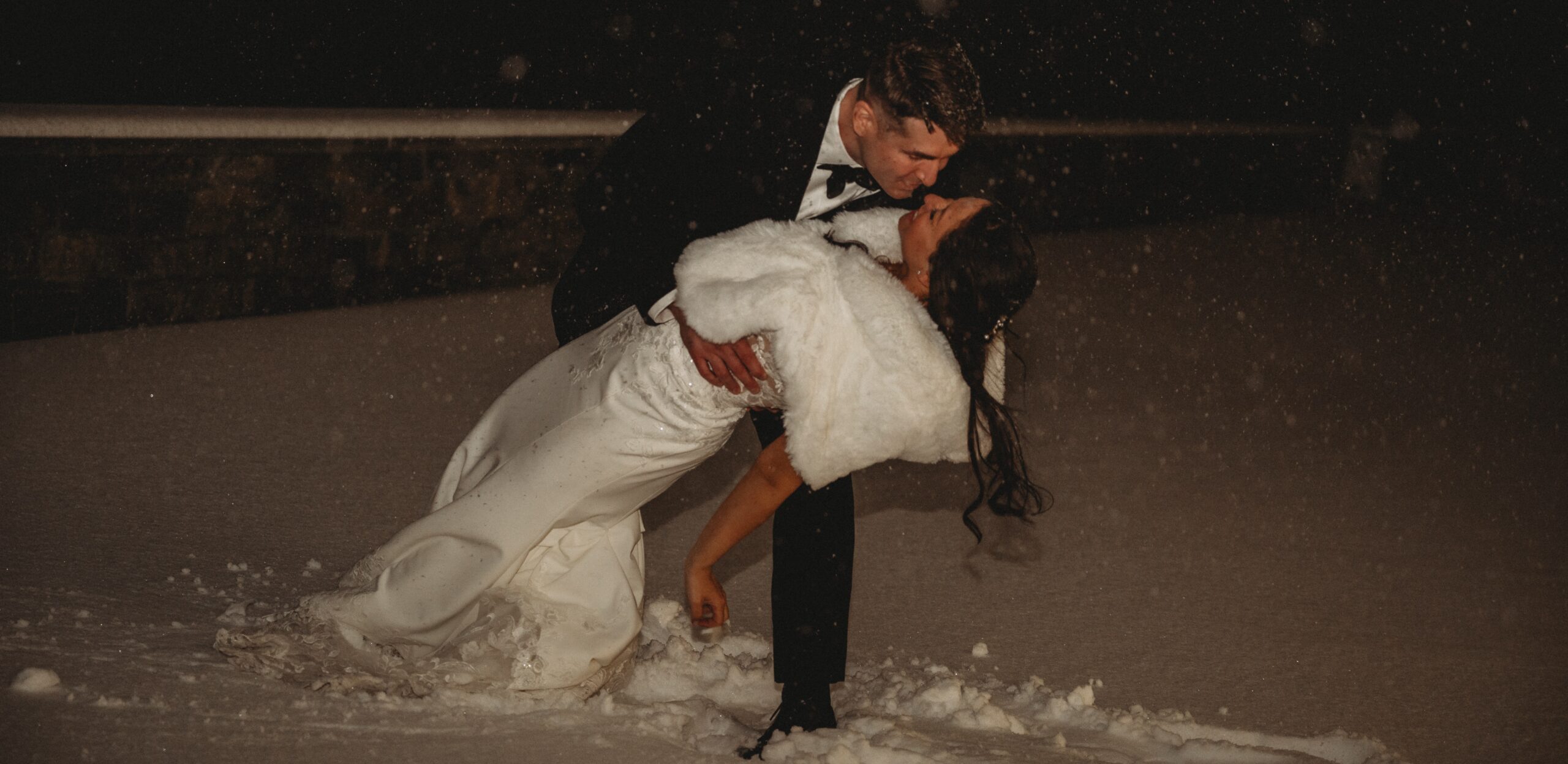 Bride and groom kissing in falling snow during winter wedding in Connecticut at Tyde at Walnut Beach